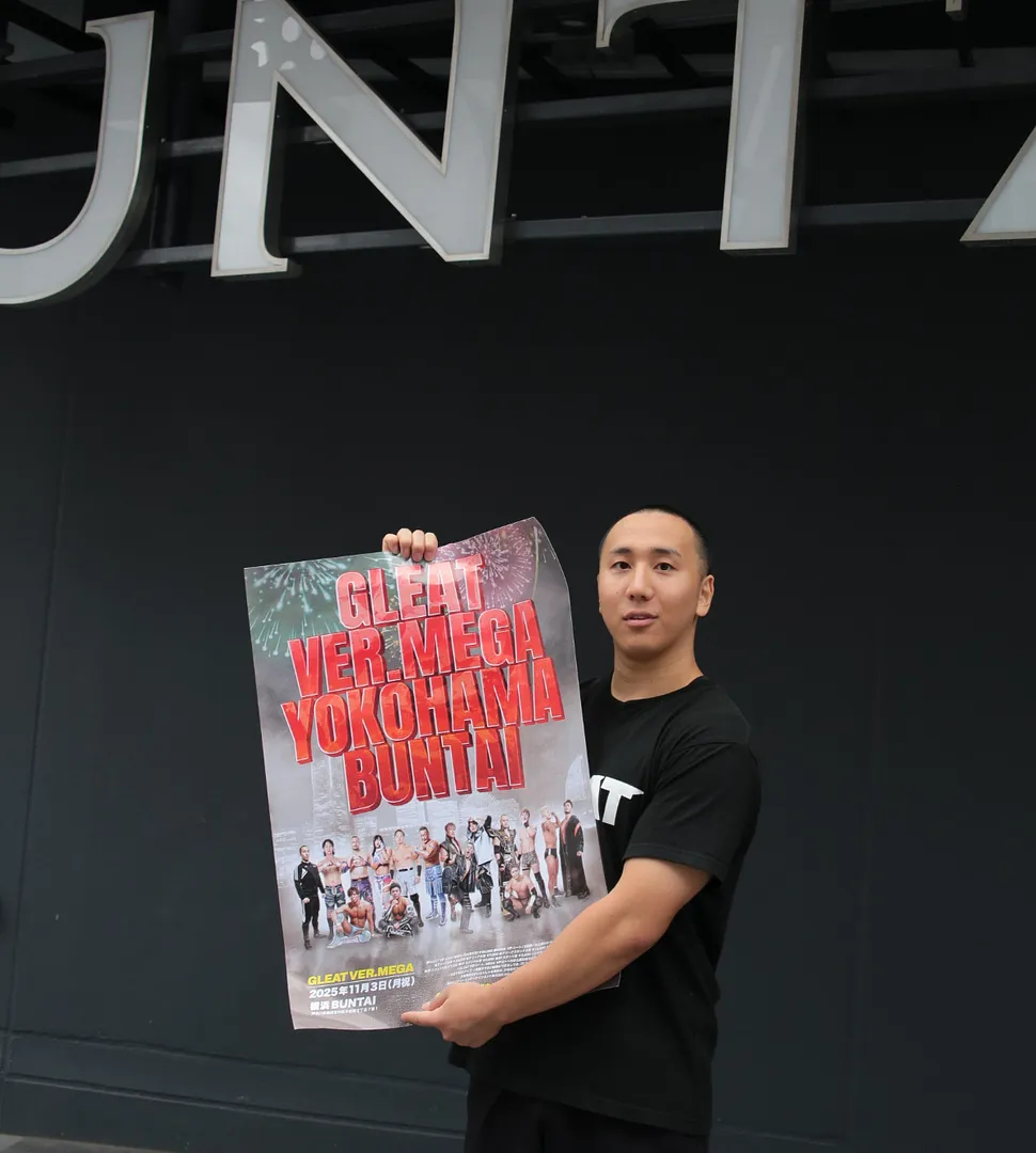 横浜ＢＵＮＴＡＩの前で大会ポスターを掲げる三宅選手