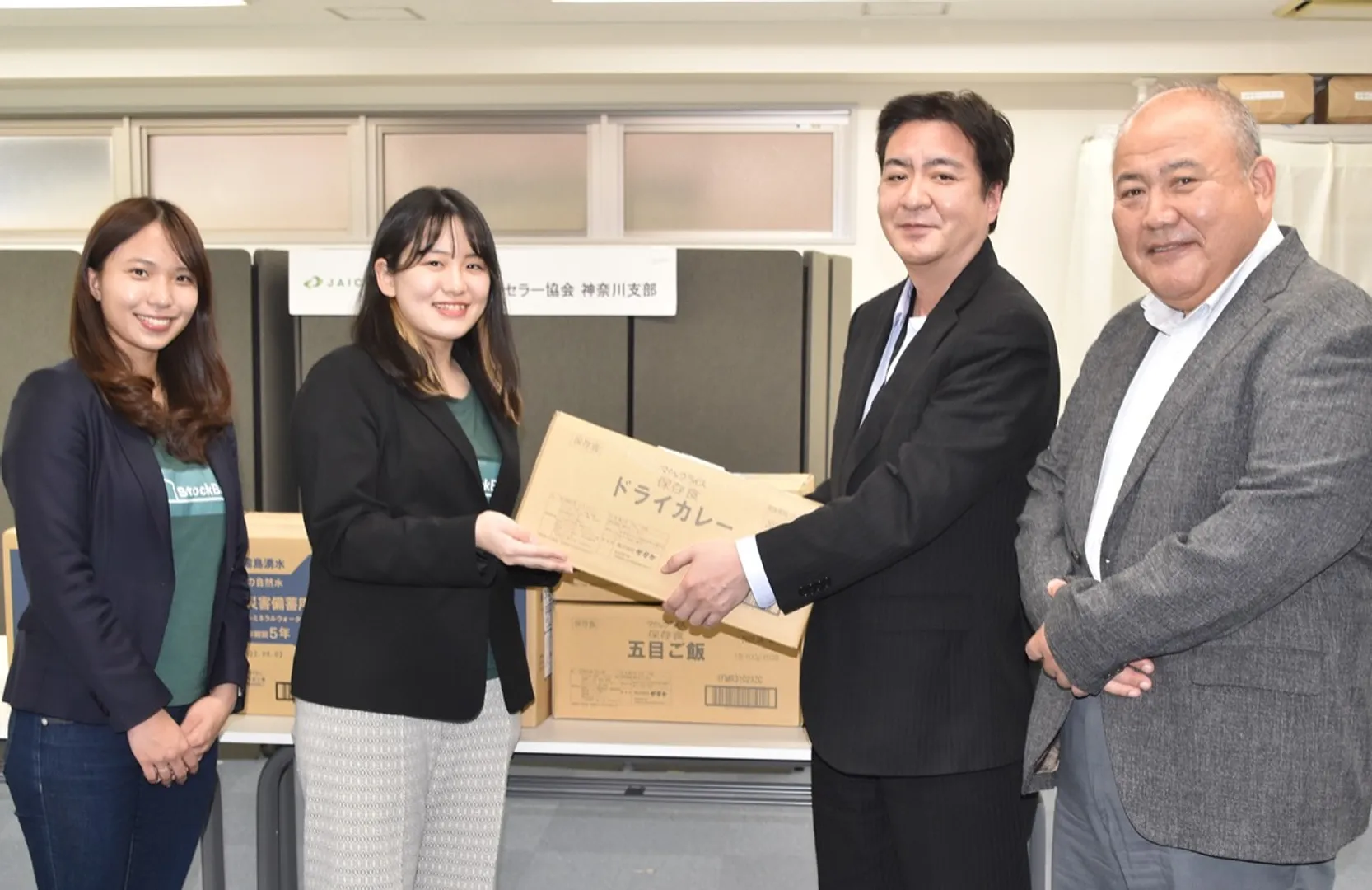 寄付する備蓄品を（株）ストックベースの関代表に手渡すカウンセラー協会の職員（右）