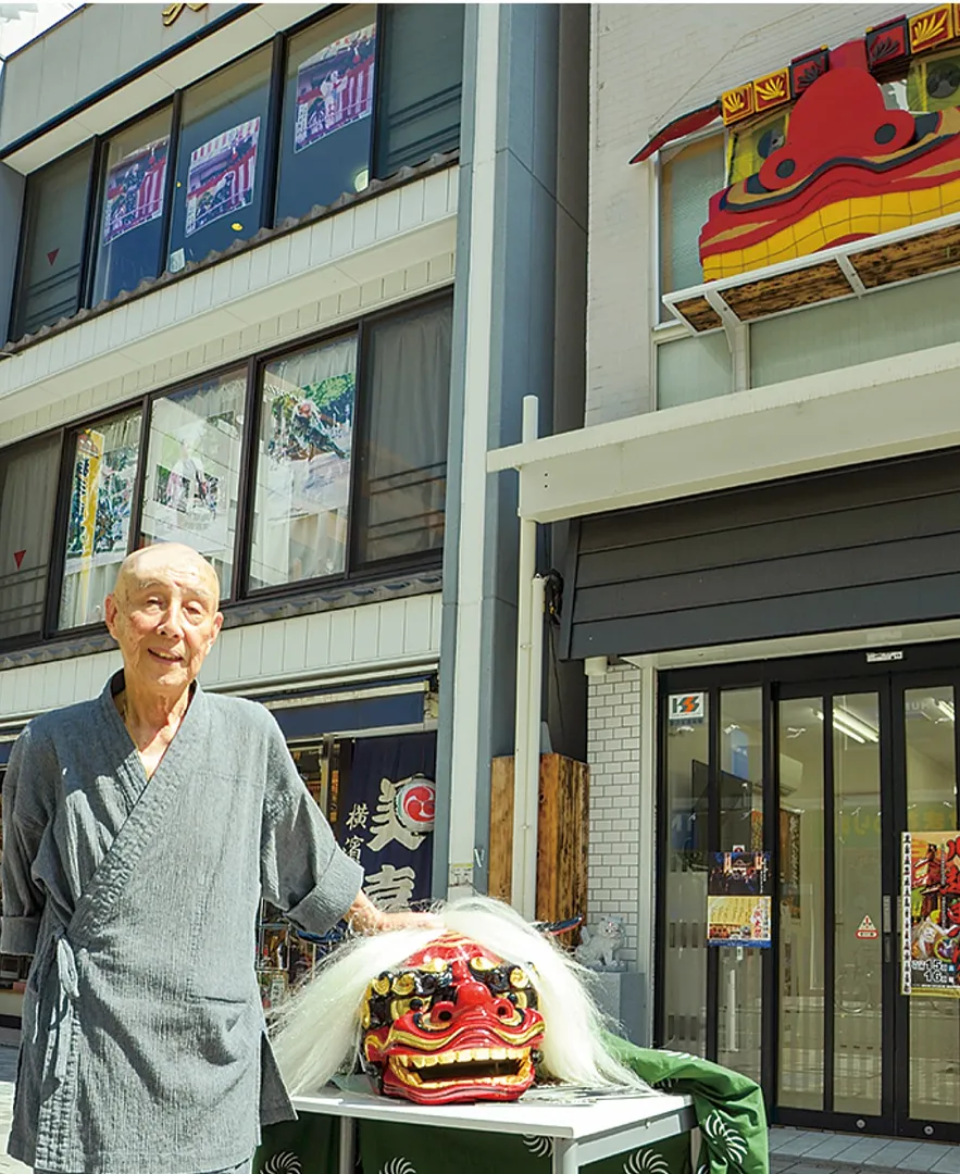 店舗＝写真左＝と獅子頭のモニュメントが掲げられた拠点の前で美濃口さん