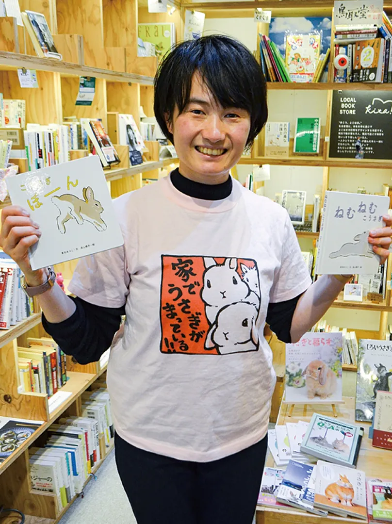 ウサギ本を手に米澤さん。「うさぎ道」のお店はブックマンション＝写真奥＝のスペース１箱分