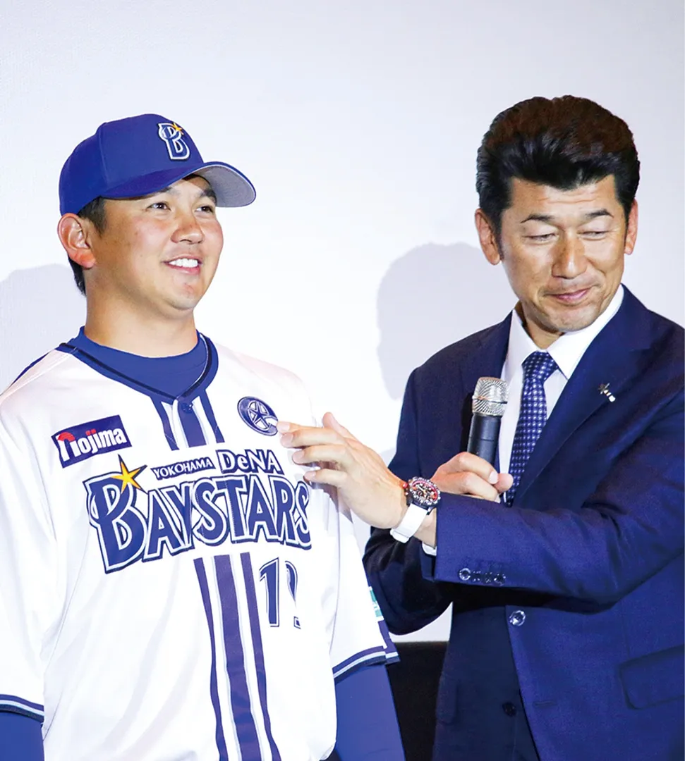 三浦監督（右）から投手キャプテンのマークを託される山﨑選手