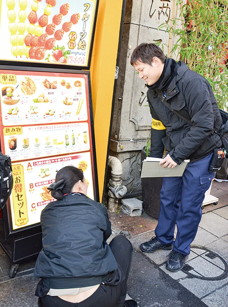不法な路上看板を店舗従業員に注意する市職員（右）